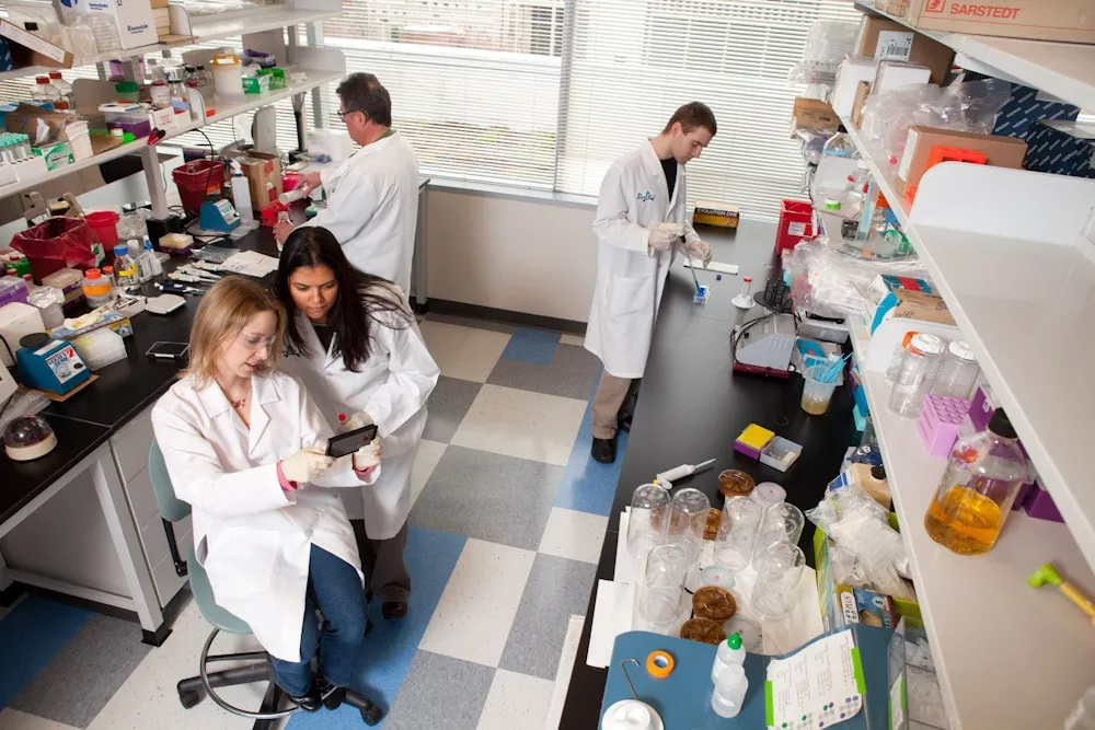 Four scientists work together inside a lab, surrounded by beakers and various equipment.